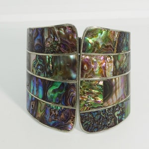 May include: A silver cuff bracelet with a geometric pattern of iridescent abalone shell pieces.