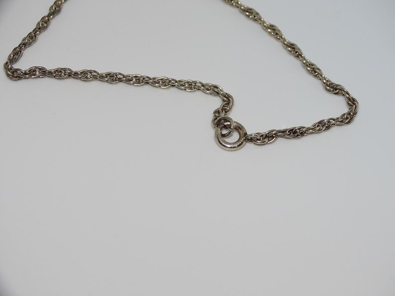 Op de afbeelding: Een zilveren ketting met een gedraaid touwontwerp en een karabijnhaak.