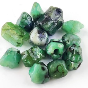 Può includere: Un gruppo di perline di pietre preziose di colore verde smeraldo, alcune con una texture ruvida e naturale, altre con una finitura liscia e lucida.