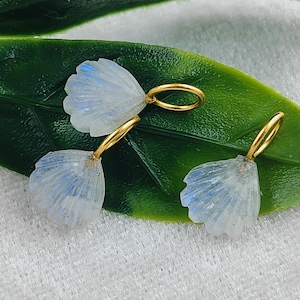 May include: Three gold-toned charms shaped like seashells with a white iridescent finish. The charms have a small gold loop at the top for attaching to a necklace or bracelet.