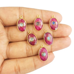 Puede incluir: Siete colgantes de forma ovalada con un engaste de oro y una piedra preciosa roja. Cada colgante tiene una piedra preciosa redonda e iridiscente más pequeña en el centro.