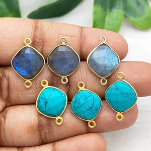 Pode incluir: Seis pingentes de pedras preciosas com engastes dourados. Três pingentes apresentam pedras de labradorita azul-acinzentado e três têm pedras turquesas. Cada pingente tem formato de losango e duas pequenas argolas.