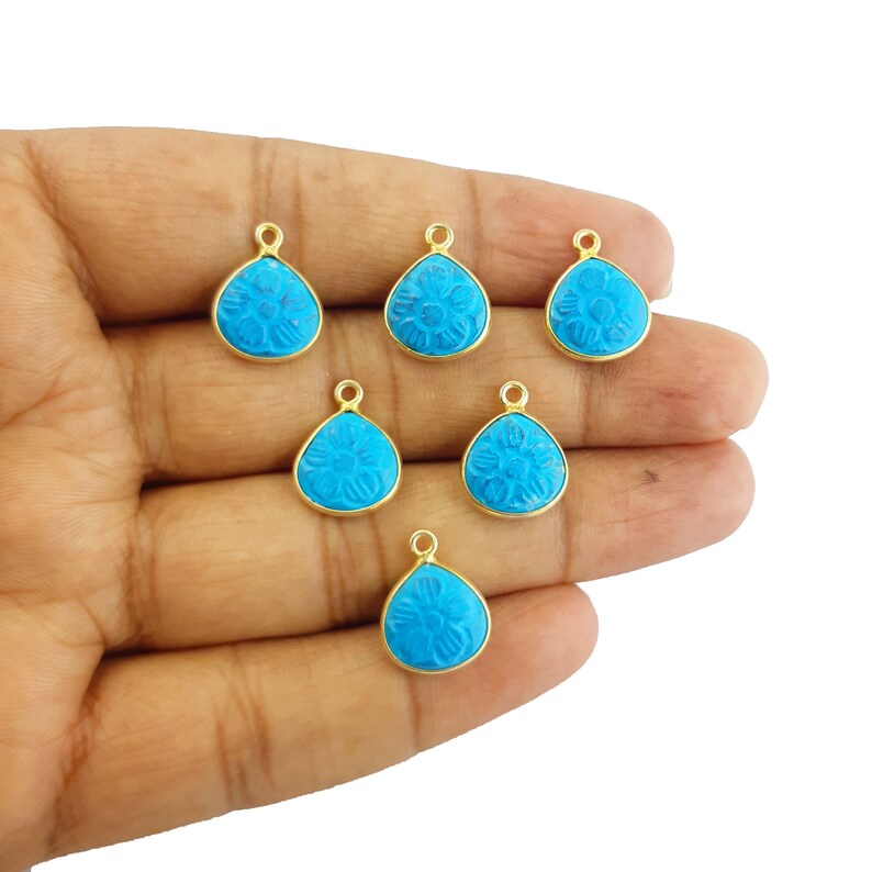 May include: Six turquoise blue gemstone pendants with gold-tone settings. Each pendant features a carved flower design.