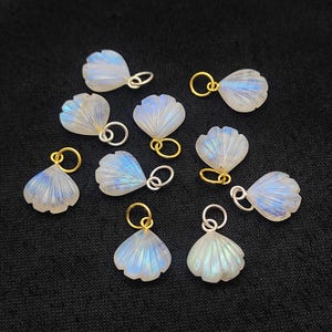 May include: Ten iridescent rainbow moonstone shell charms with gold and silver jump rings. The charms are shaped like seashells and have a pearly white colour with a rainbow sheen.