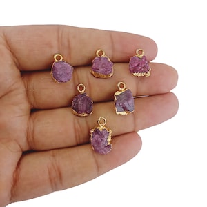 May include: Seven pink and gold gemstone charms with a gold loop for hanging. The charms are irregularly shaped and have a rough, natural look.