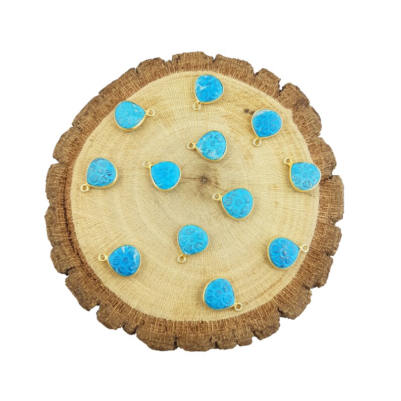 May include: A collection of 12 turquoise blue gemstone pendants with gold-plated bail. Each pendant features a carved floral design and is shaped like a teardrop.