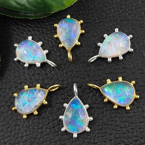 May include: Six teardrop-shaped opal pendants with gold and silver settings. The pendants have a beaded edge and a loop for attaching to a chain or cord.