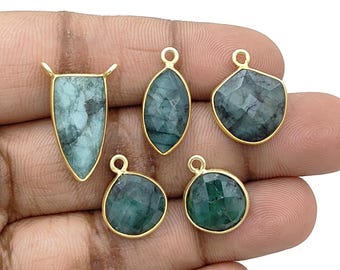 May include: Five gold-plated pendants with emerald-green gemstones in various shapes: a shield, an oval, a faceted irregular shape, a rounded triangle, and a circle. Each pendant has a loop for hanging.