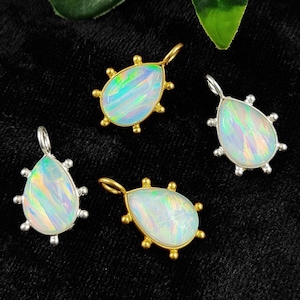 May include: Four teardrop-shaped opal pendants with gold and silver settings. The opals are iridescent and have a white, blue, and green colour.