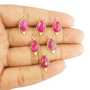 Peut inclure: Six pendentifs en forme de goutte d'eau plaqués or avec des pierres précieuses de rubis rouges. Chaque pendentif a une petite boucle en haut pour l'attacher à une chaîne ou un cordon.