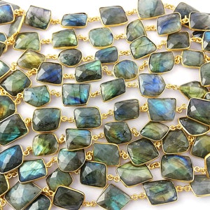 May include: A long strand of labradorite gemstone beads, each bead is faceted and has a rectangular shape. The beads are strung on a gold chain.