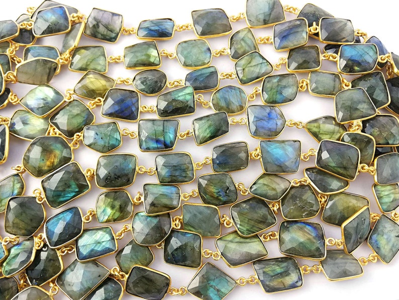 May include: A long strand of labradorite gemstone beads, each bead is faceted and has a rectangular shape. The beads are strung on a gold chain.