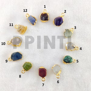 May include: A collection of twelve gemstone pendants with gold-colored metal edging. The gemstones vary in color, including purple, green, blue, and yellow. Each pendant has a small loop for attaching to a chain or other jewelry component.
