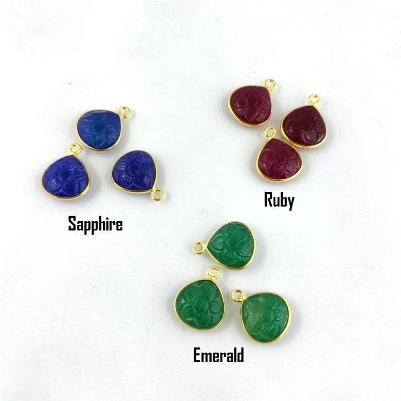May include: Three sets of gemstone pendants, each set featuring three pendants. The pendants are shaped like teardrops and have a carved flower design. The gemstones are sapphire, ruby, and emerald.
