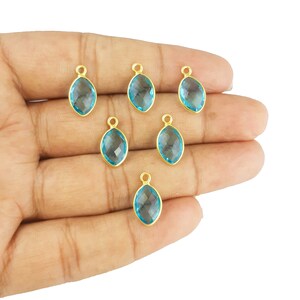 May include: Six gold-plated pendant charms with light blue faceted gemstone inserts. Each charm has a loop for attaching to a necklace or bracelet.