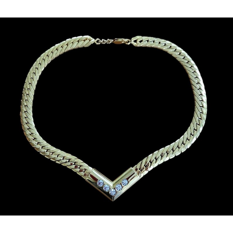 May include: A gold chain necklace with a V-shaped pendant set with five clear rhinestones.