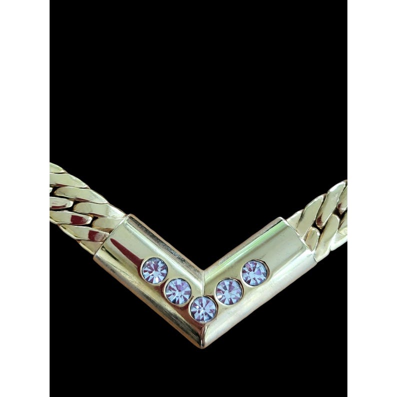 May include: A gold chain necklace with a V-shaped pendant adorned with five clear rhinestones.