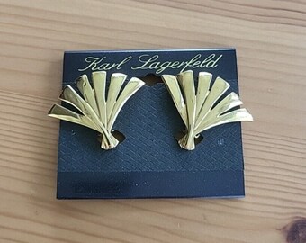 May include: A pair of gold-tone fan-shaped earrings on a black card with the text "Karl Lagerfeld" printed on it.
