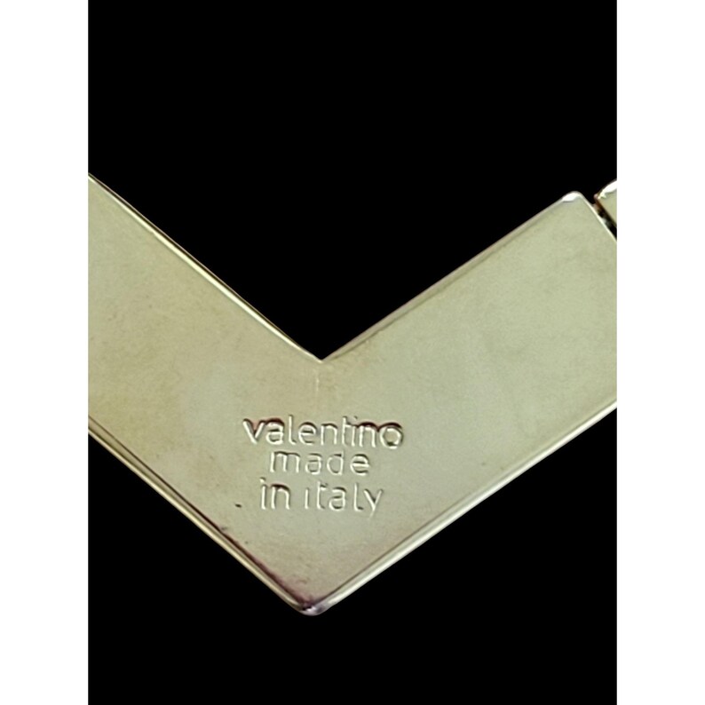 May include: Close-up of a silver metal tag with the text "valentino made in italy" engraved on it.