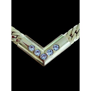 May include: A gold chain necklace with a V-shaped pendant set with five clear rhinestones.