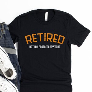 May include: A black t-shirt with the text "Retired Not My Problem Anymore" in orange and white lettering.