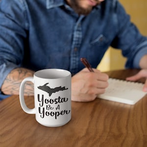 May include: White ceramic coffee mug with a black silhouette of the Upper Peninsula of Michigan and the text "Yoopsta Be A Yooper".