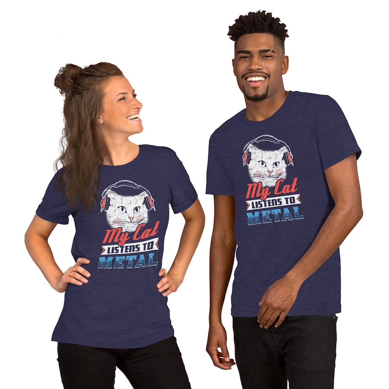 May include: Two people wearing navy blue t-shirts with a white cat wearing headphones and the text "My Cat Listens To Metal".