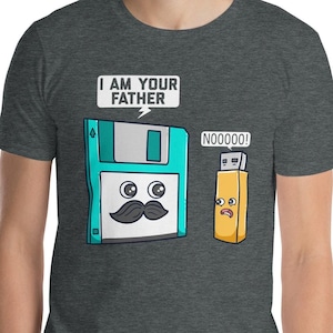 Pode incluir: Uma camiseta cinza escura mesclada com um gráfico humorístico de um disquete com bigode que diz "Eu sou seu pai" para uma unidade USB de aparência triste que diz "NOOOO!"