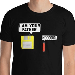 Pode incluir: Camiseta preta com um gráfico engraçado. Um disquete amarelo diz "I AM YOUR FATHER" e uma unidade USB vermelha exclama "NOOOO!" em texto branco. A camiseta é de manga curta.