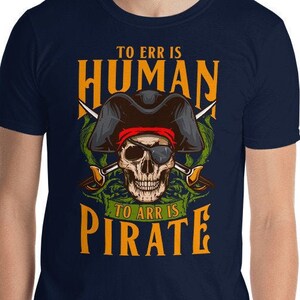 Può includere: T-shirt blu navy con un design a tema pirata. Il design presenta un teschio con cappello da pirata e occhiali da sole, con spade incrociate. Il testo recita "TO ERR IS HUMAN, TO ARR IS PIRATE" in arancione e verde.