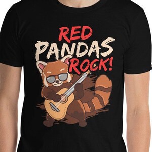Puede incluir: Camiseta negra con un panda rojo de dibujos animados con gafas de sol y tocando la guitarra. El texto "RED PANDAS ROCK!" está encima del panda. La camiseta está hecha de un material suave.
