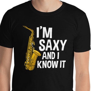 Puede incluir: Camiseta negra con un diseño de saxofón dorado y el texto blanco "I'M SAXY AND I KNOW IT". Esta prenda informal está hecha de una tela suave. Una prenda de temática musical, perfecta para los amantes de la música.