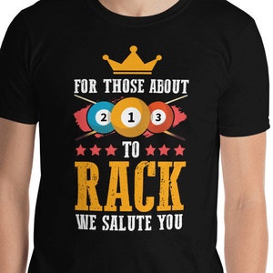 May include: Black t-shirt with a white crown and the text "For those about to rack, we salute you". The text is surrounded by a red, white, and blue design with billiard balls.