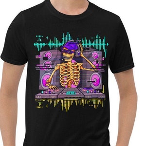 May include: Black t-shirt featuring a colorful graphic of a skeleton DJ wearing headphones and a hat, playing music on turntables. The design includes sound wave elements and speakers, creating a vibrant, musical theme.
