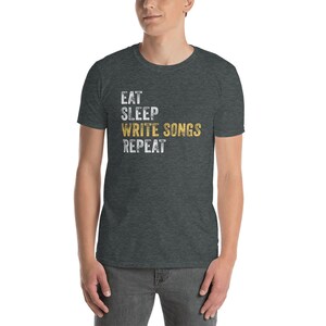 Puede incluir: Una camiseta gris oscuro jaspeada con el texto "Eat Sleep Write Songs Repeat" en letras blancas y doradas.
