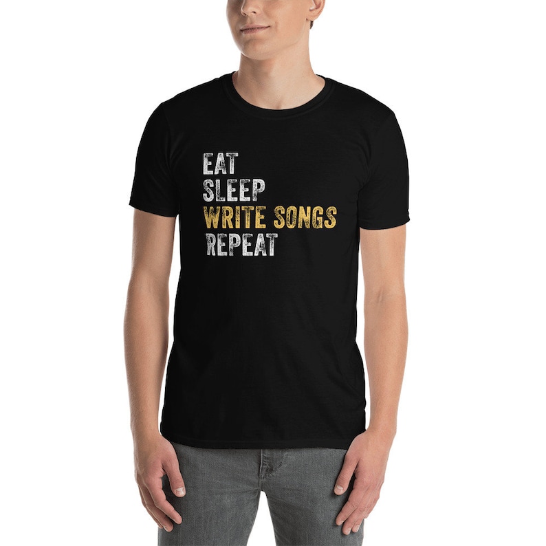 Puede incluir: Camiseta negra con texto blanco que dice "Eat Sleep Write Songs Repeat" en una fuente desgastada. La palabra "Write Songs" est&aacute; en amarillo.