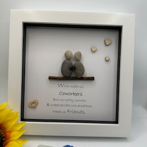 May include: A framed artwork with a white border features a pebble art scene of two figures on a twig, with wooden heart accents. Text reads "Work made us Coworkers, But our potty mouths & inappropriate conversations Made us Friends."