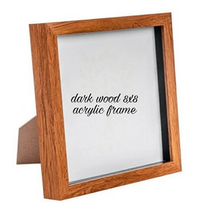 May include: Dark wood 8x8 acrylic frame. The frame has a brown wood finish and a black mat. The frame is standing on a white surface.