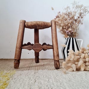 Peut inclure: Un petit tabouret en bois à trois pieds avec une assise ronde tressée en corde de fibre naturelle. Le tabouret présente une finition en bois brun foncé et une structure de support décorative festonnée reliant les trois pieds à la base.