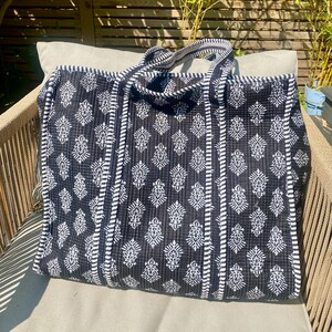 Pu&ograve; includere: Una grande borsa tote bianca e nera con un motivo floreale. La borsa ha due manici ed &egrave; su una sedia. La borsa &egrave; realizzata in tessuto trapuntato e presenta un design a righe sui lati.