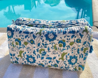 Può includere: Una trousse da trucco in cotone bianco con stampa floreale blu e verde. La trousse ha una chiusura a zip e un pon pon.