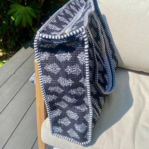 Pu&ograve; includere: Una borsa tote nera e bianca con un motivo a foglie. La borsa ha un bordo a righe e una chiusura a cerniera. La borsa &egrave; realizzata in tessuto trapuntato ed &egrave; appoggiata su una sedia.