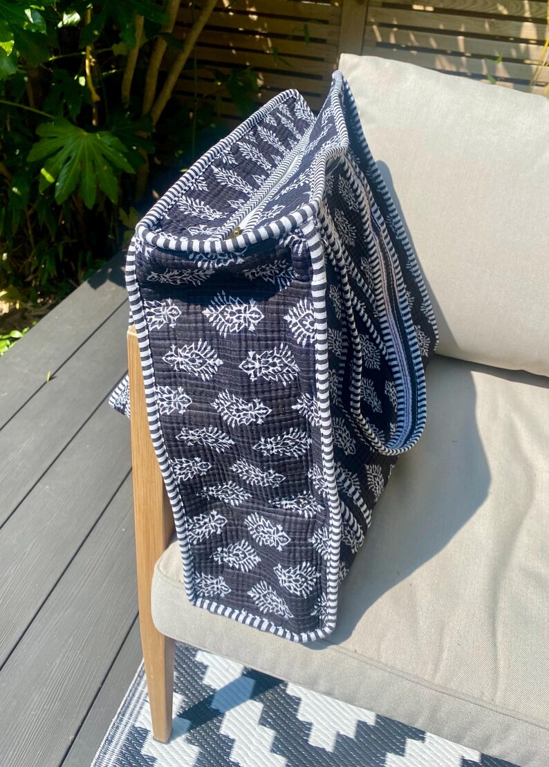 Pu&ograve; includere: Una borsa tote nera e bianca con un motivo a foglie. La borsa ha un bordo a righe e una chiusura a cerniera. La borsa &egrave; realizzata in tessuto trapuntato ed &egrave; appoggiata su una sedia.