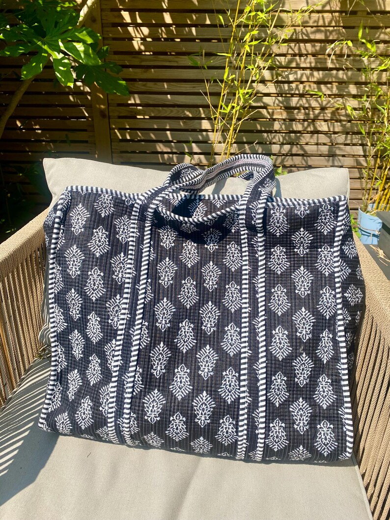 Pu&ograve; includere: Una grande borsa tote bianca e nera con un motivo floreale. La borsa ha due manici ed &egrave; su una sedia. La borsa &egrave; realizzata in tessuto trapuntato e presenta un design a righe sui lati.