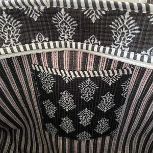 Pu&ograve; includere: Una borsa tote trapuntata in bianco e nero con un motivo floreale e dettagli a righe. La borsa &egrave; dotata di chiusura a zip e una tasca interna. Il design combina motivi floreali e a righe, creando un accessorio elegante.