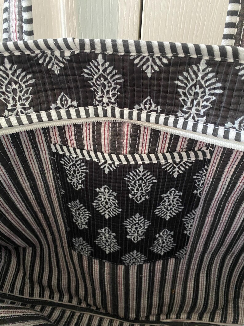 Pu&ograve; includere: Una borsa tote trapuntata in bianco e nero con un motivo floreale e dettagli a righe. La borsa &egrave; dotata di chiusura a zip e una tasca interna. Il design combina motivi floreali e a righe, creando un accessorio elegante.