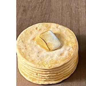 May include: A stack of round, light yellow objects, possibly pancakes or tortillas, topped with a square, light-colored object. The items are on a brown surface.