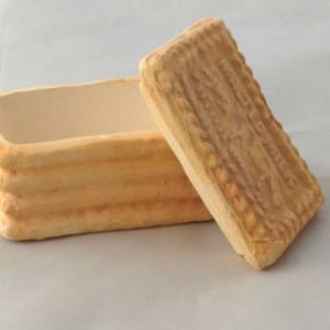 Może przedstawiać: Ceramiczne pudełko na ciasteczka z pokrywką w kształcie ciasteczka. Pudełko jest beżowe i ma fakturowaną powierzchnię.