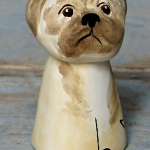 May include: A hand-painted ceramic figurine of a pug dog. The figurine is white with brown accents and has a realistic depiction of a pug's face.
