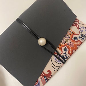 Può includere: Una pochette in tessuto nero con un motivo floreale all'interno. La pochette ha una tracolla nera con un bottone di perla.
